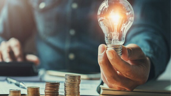 Business man holding light bulb on the desk in office and calculating on calculator