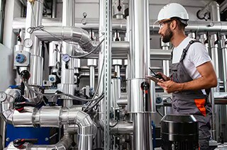 An engineer at work with the pipes while holding a walkie takie and a mobile