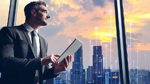 A man looking out of the window with a tablet in hand overlaid with graphics of transmission nodes