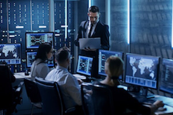 A group of colleagues working on desktops, while a man stands and works on a laptop